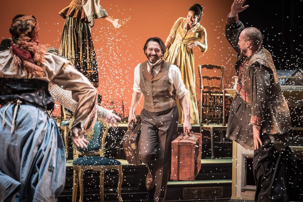 David as Levin, laughing as he carries two suitcases through falling snow, in Anna Karenina