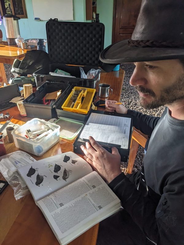 David on Isla San Cristóbal in the Galápagos, recording data on a clipboard beside an open bird guide
